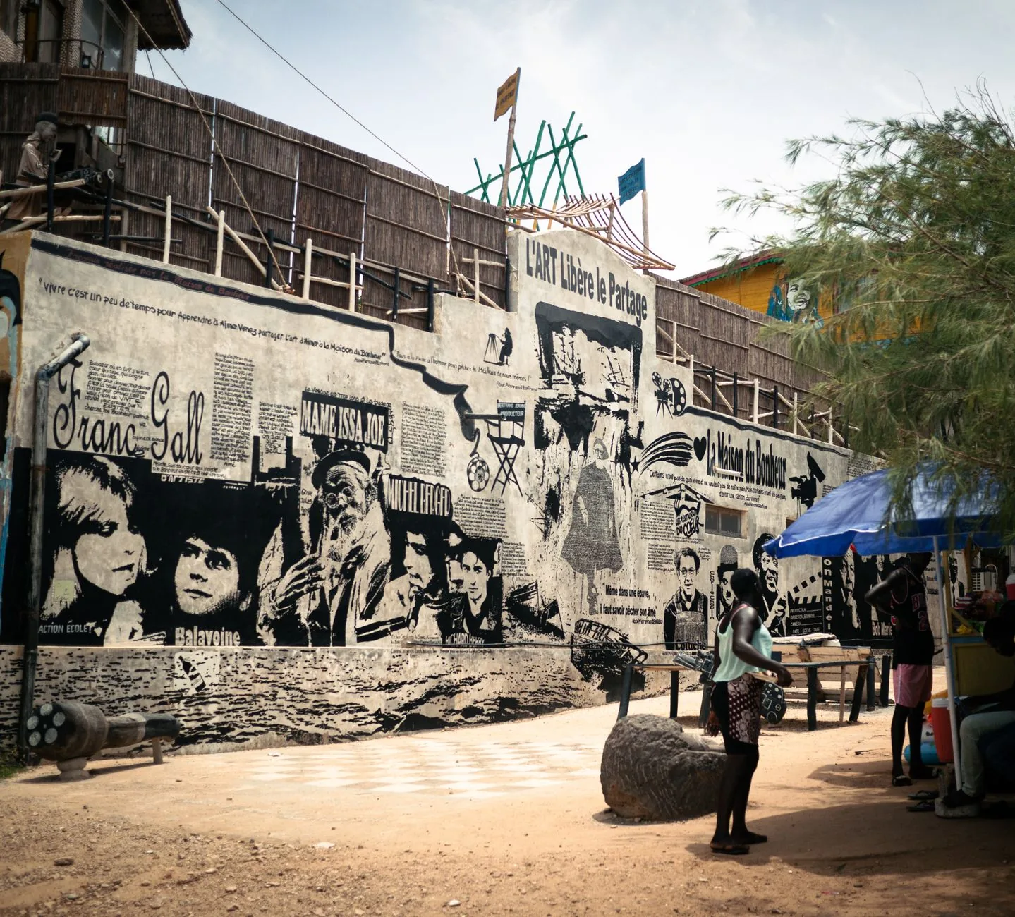 Mur de street art noir et blanc représentant des visages historiques sénégalais avec textes et symboles