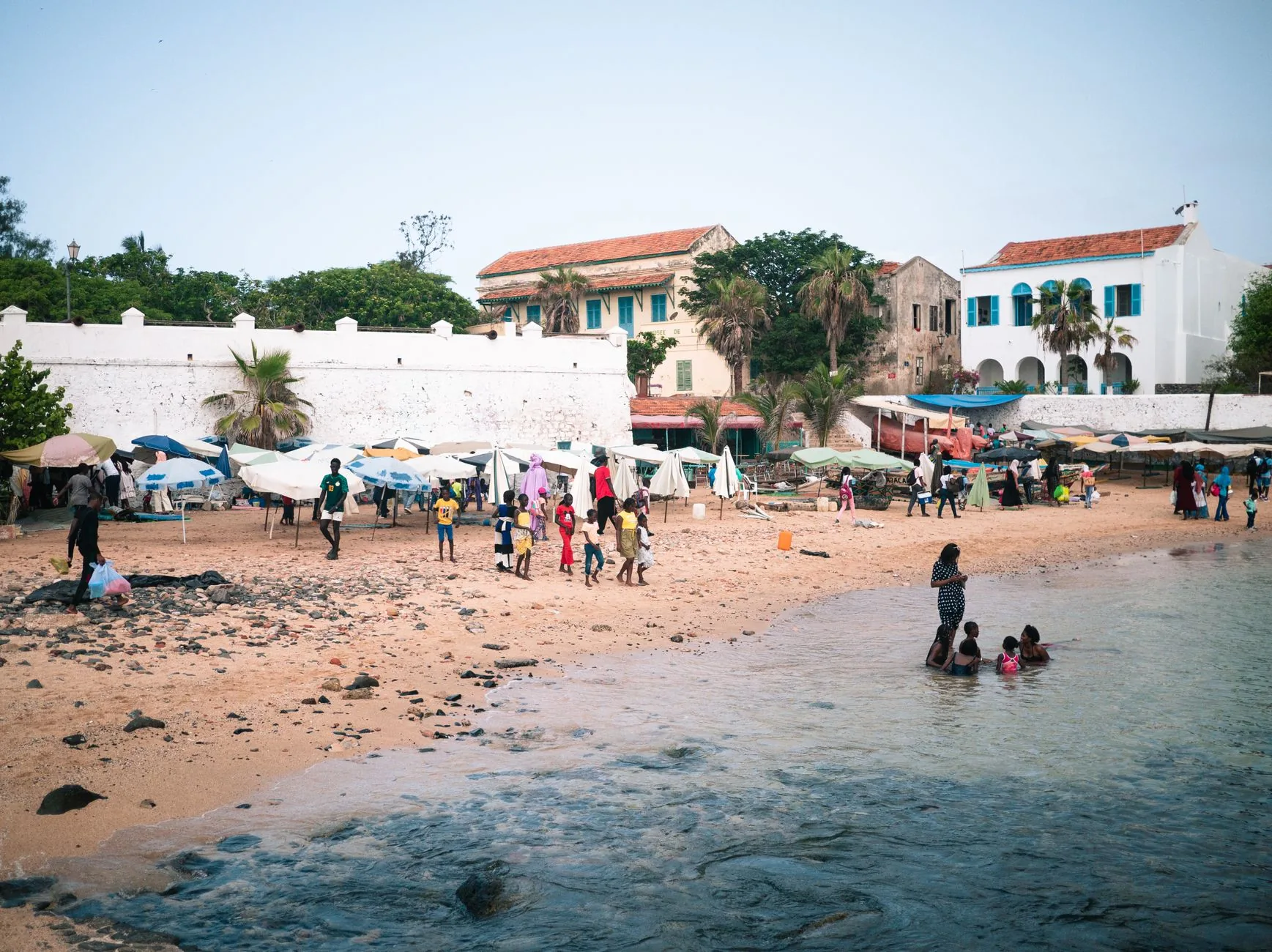 Plage sénégalaise animée avec familles baignant près de bâtiments coloniaux blanchis