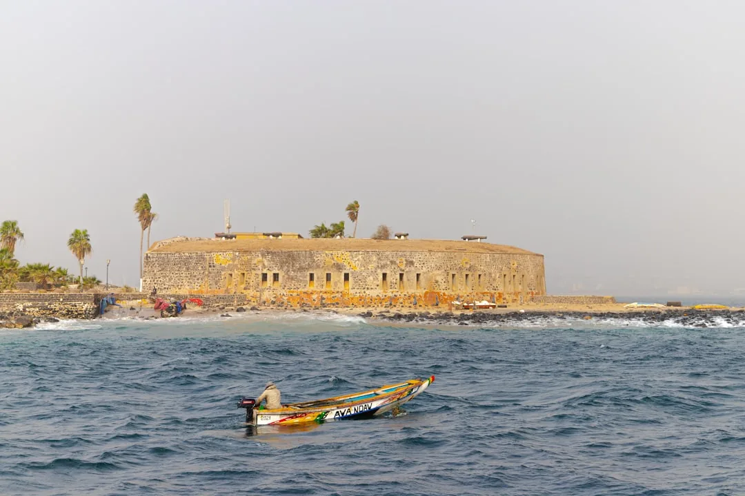 Barque de pêche colorée devant fort colonial historique à Dakar avec palmiers