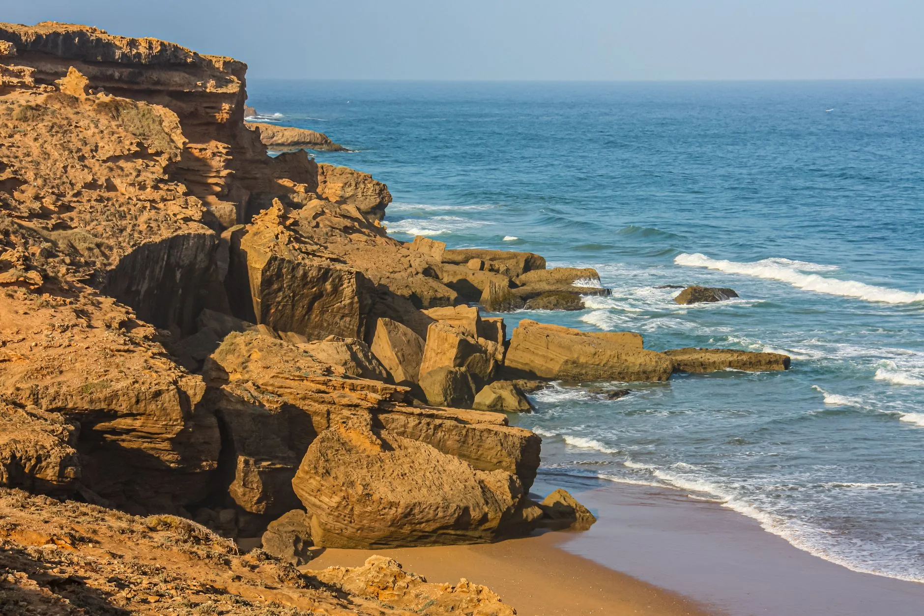 Falaises rocheuses ocre surplombant une mer bleue aux vagues écumantes