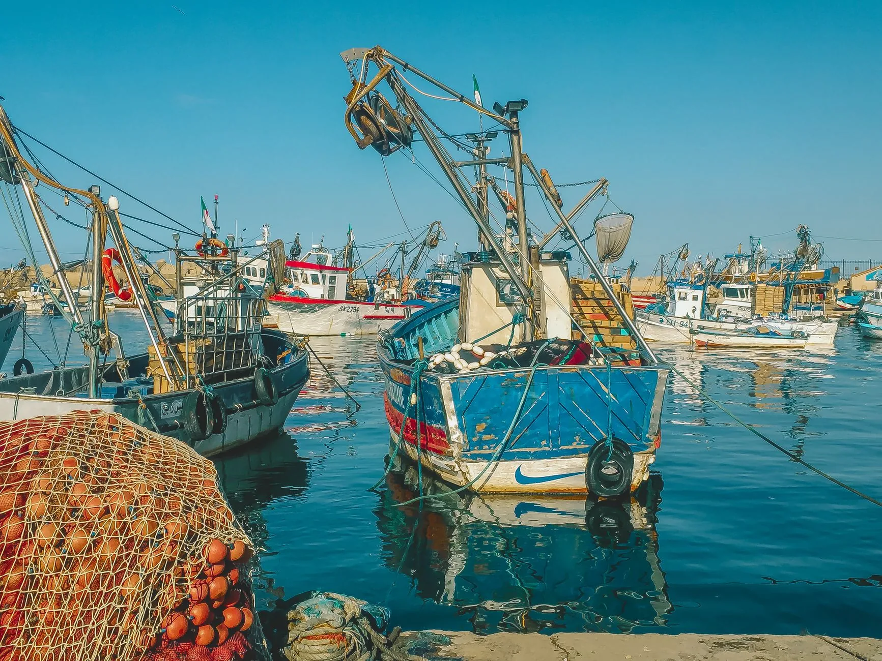 Bateaux de pêche colorés amarrés dans un port, filets de pêche oranges au premier plan
