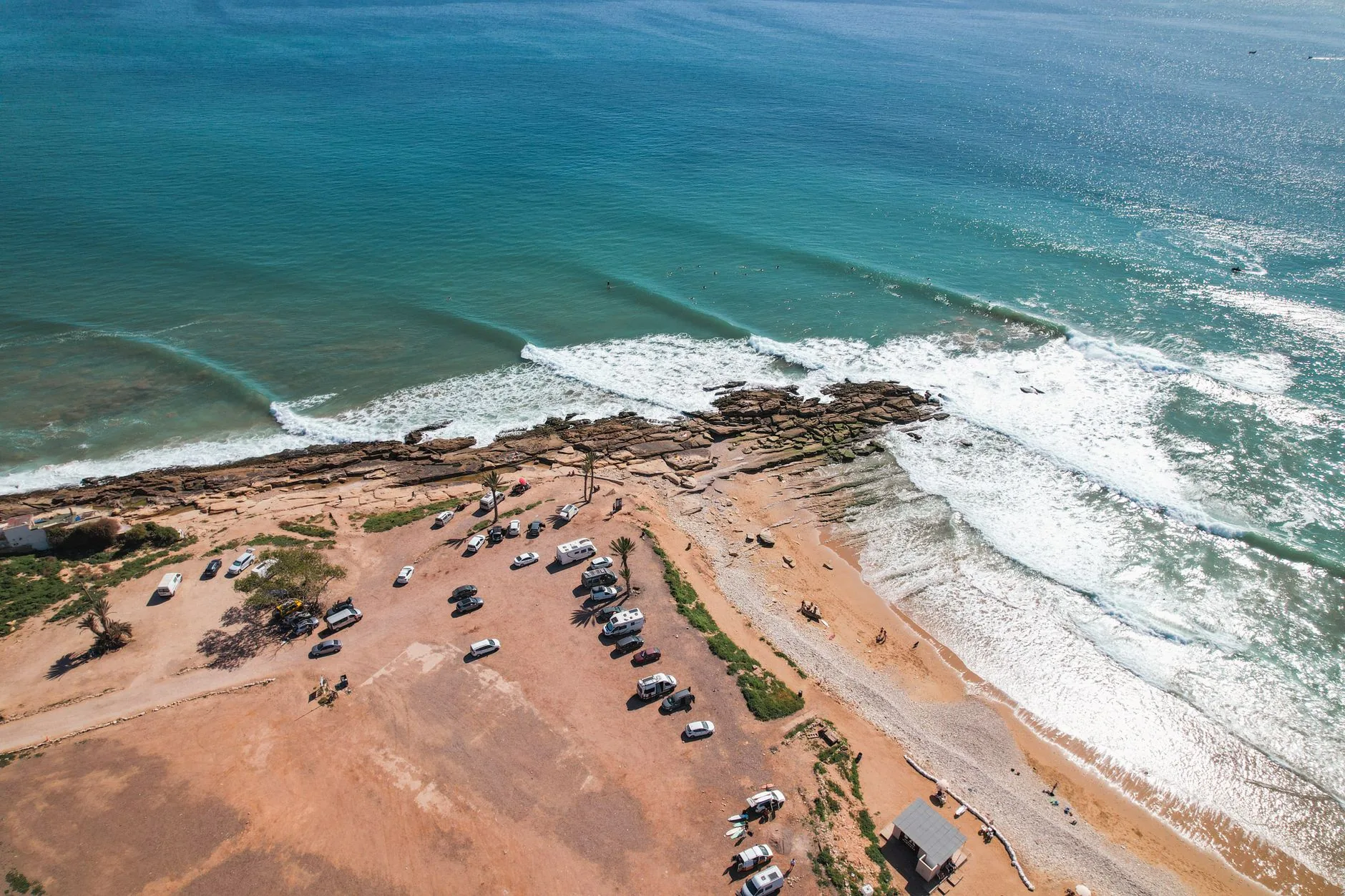 Vue aérienne d'une plage rocheuse avec véhicules garés et vagues déferlantes