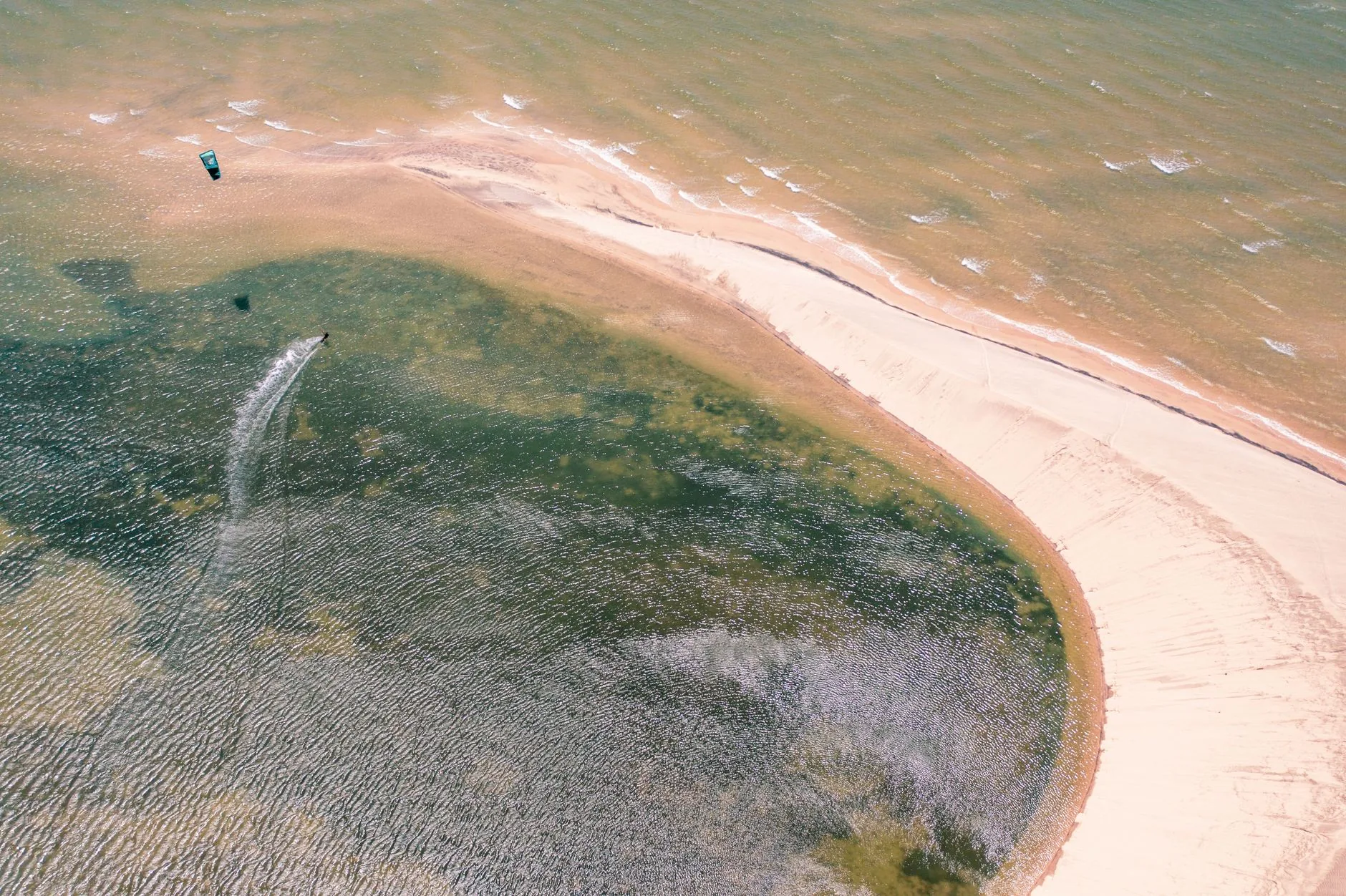 Vue aérienne d'un kitesurfeur glissant sur un lagon côtier aux eaux peu profondes bordé d'une langue de sable