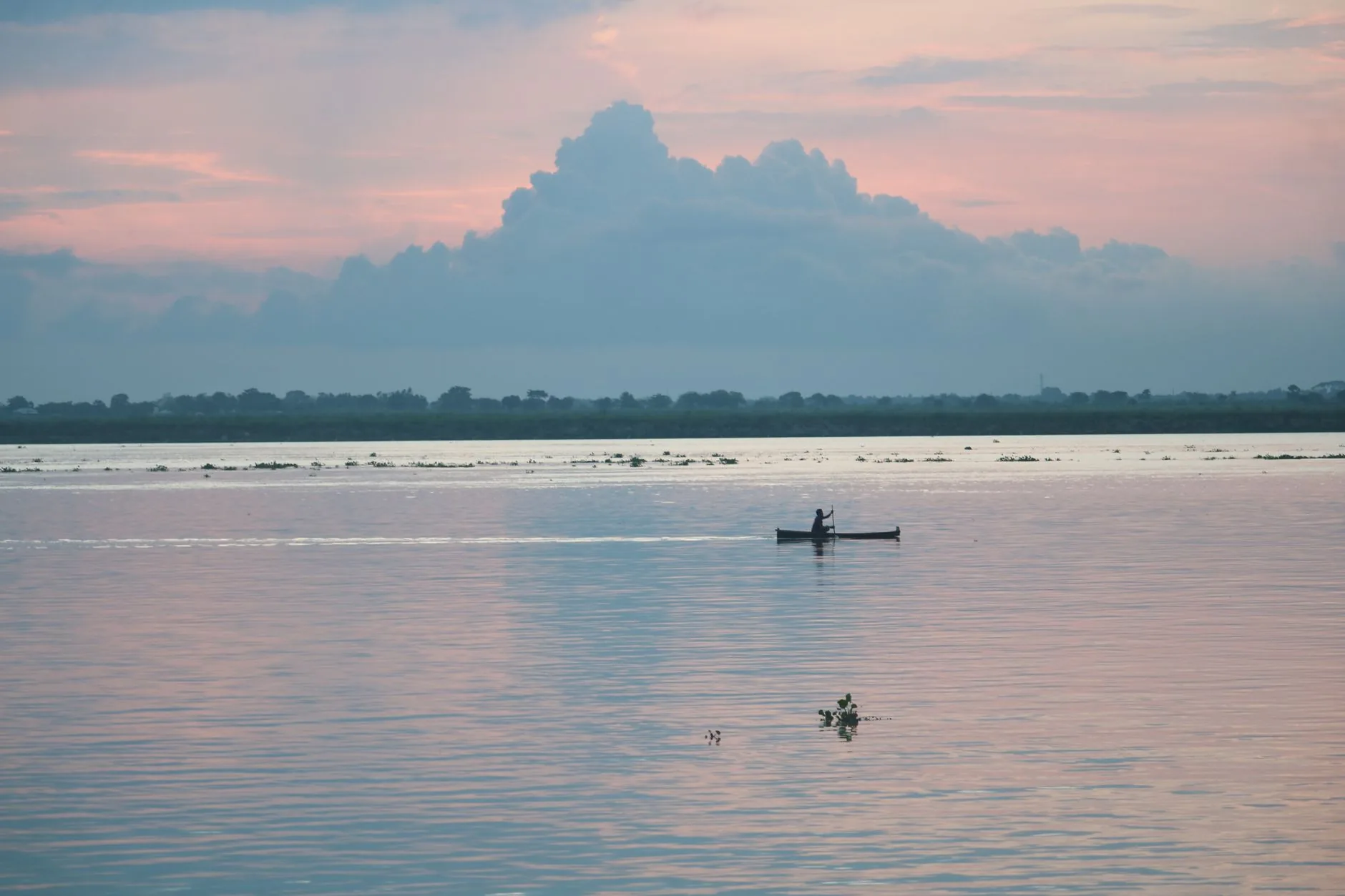 Silhouette d'un piroguier pagayant seul sur un fleuve au coucher du soleil