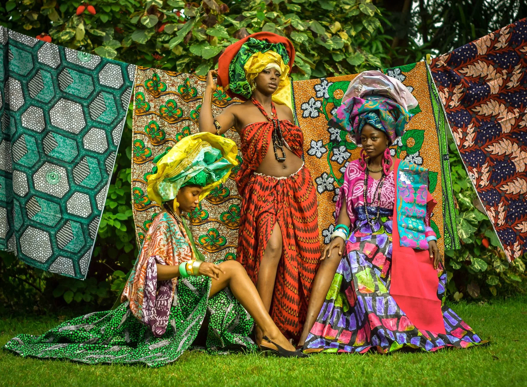 Trois femmes en tenues et coiffes de tissus imprimés colorés dans un jardin