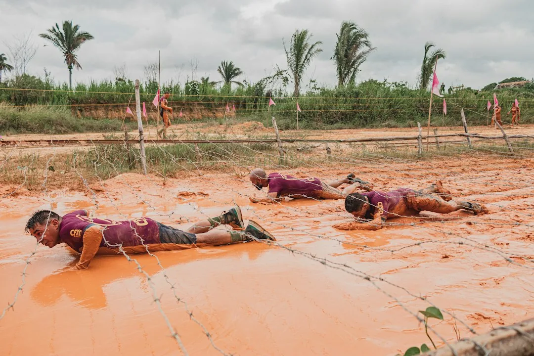 Participants rampant dans la boue sous des fils barbelés lors d'une épreuve sportive en plein air
