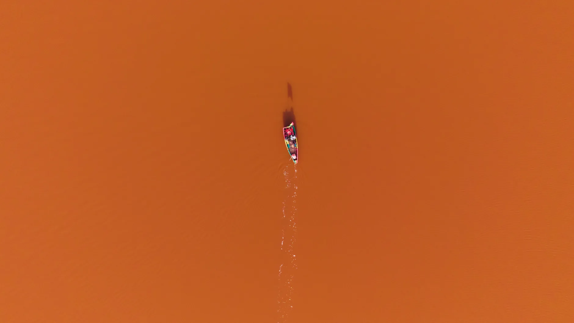 Vue drone d'un canoë coloré glissant sur les eaux orange du lac Retba au Sénégal